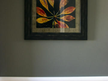 A framed art photograph of flowers hands on the wall. Below it is a side table, empty except for a dustrag