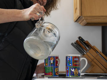 A middle aged woman pours water from a kettle into two Christmas mugs