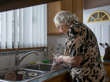 An elderly woman washes dishes at a sink