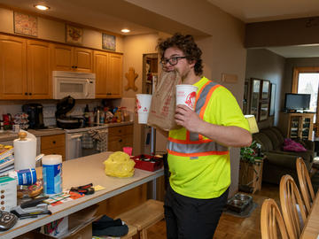 A young man in a reflective safety shirt holds a Wendy's cup in either hand, and a brown paper fast food bag in his teeth