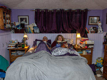 A middle-aged couple sit together in bed reading