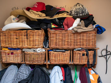 A cluttered assortment of jackets hanging on hooks and wicker baskets with hats and gloves spilling out of them