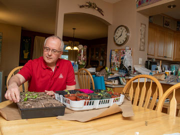 A man sits at a table with a collection of sprouted herbs in small pots.
