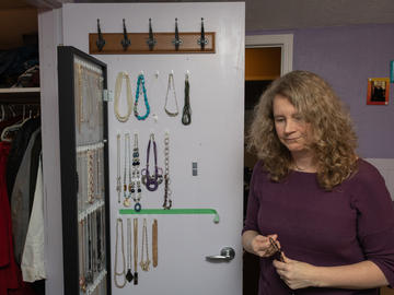 A woman stands beside her closet door. There are severl rows of hooks with necklaces hung on them on the door.