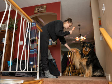A young woman grooms a dog on the landing in a house. The dog's paw is in the woman's hand.