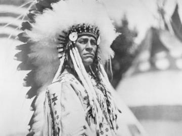 Photo of Chief Buffalo Child Long Lance wearing headdress with tipis in background