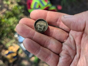 A researcher holds a small metal object that was found on the dig.