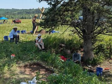 Archaeologists sit on the ground amidst the equipment.