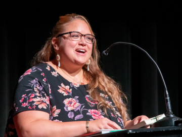 Francine Cunningham speaks at a lectern in a dark theatre.