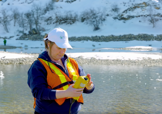 Dr. Tricia Stadnyk reads a water sampling monitor outside next to a river.