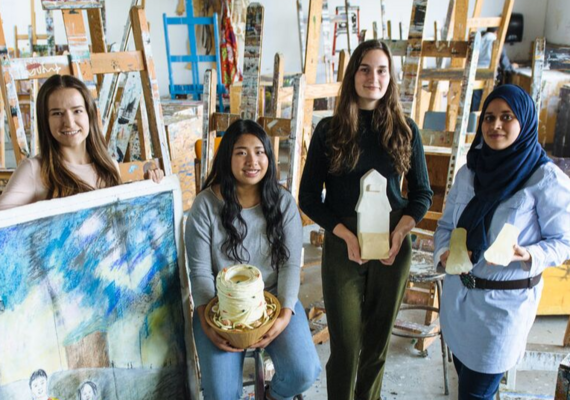 students holding their paintings in an art studio