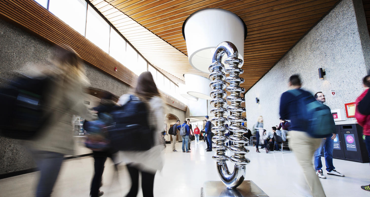 Katie Ohe's Zipper sculpture in Science Theatres is in the centre of the photo. Students in motion walk around it.
