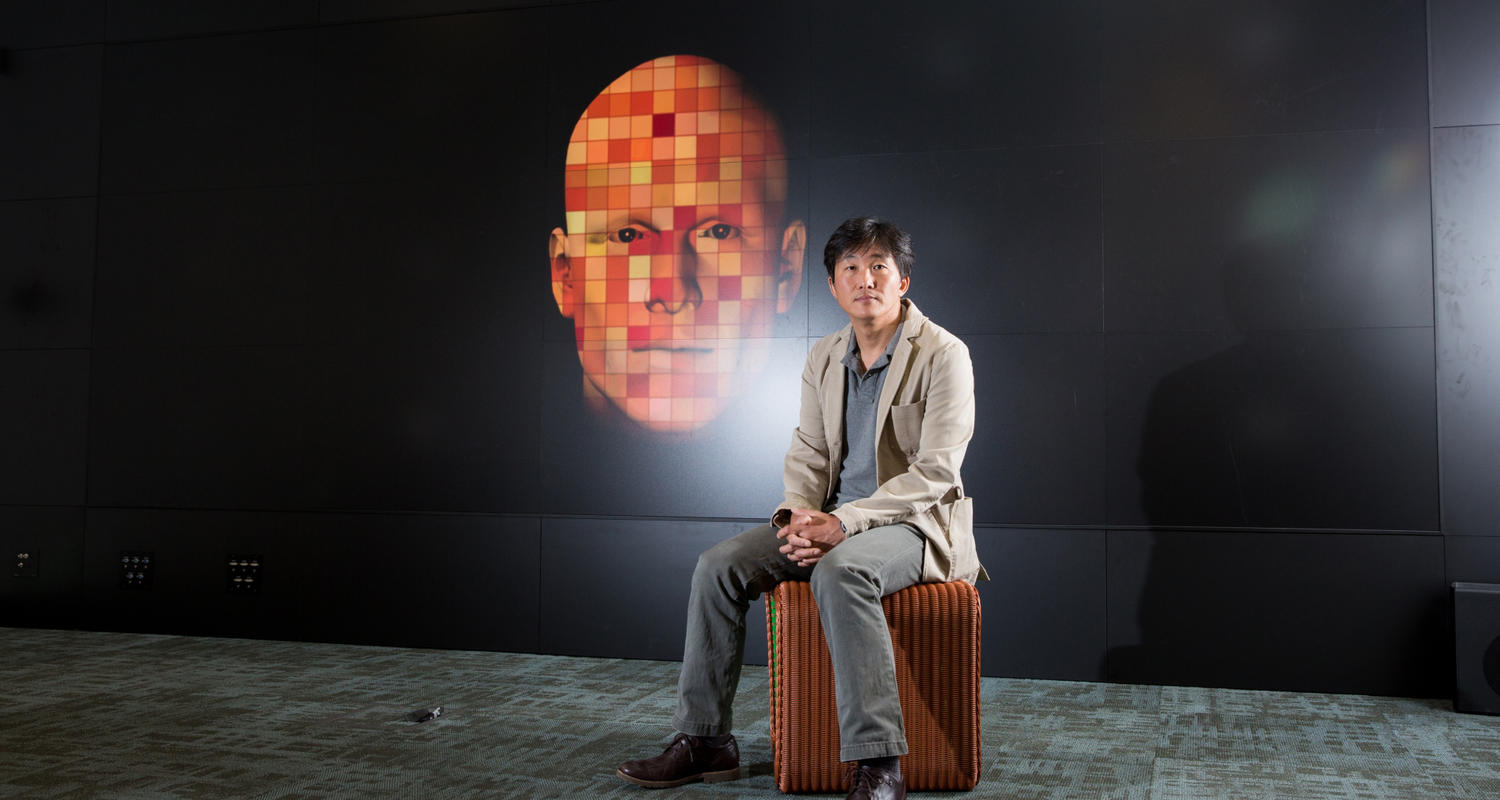 Psychology researcher Kibeom Lee sits on a chair in front of a large graphic post of a face