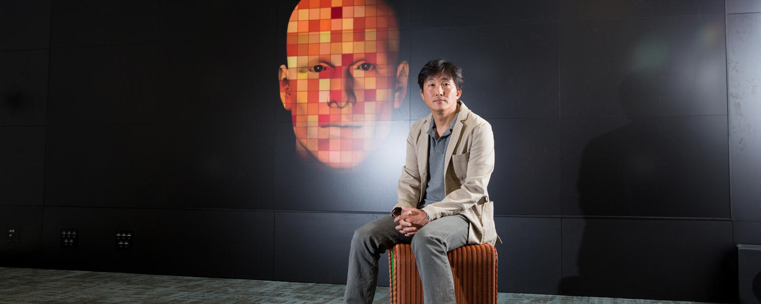 Psychology researcher Kibeom Lee sits on a chair in front of a large graphic post of a face