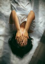 Woman laying on the bed with hands over her face