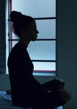 Woman sitting on the edge of her bed in the dark