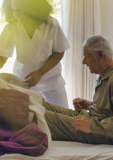 Stock photo of nurse helping elderly man into bed