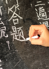 A stock image of a person's hand writing in Chinese on a blackboard