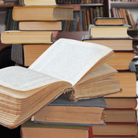 A pile of books on a table in front of a bookshelf