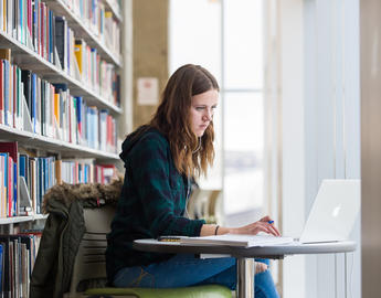 A student hunches over a laptop in the libary