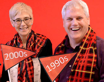 Arts alumni throughout the decades pose with flags that say 2000s and 1990s