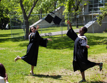 Two female students throw their convocation mortarboards in the air in celebration