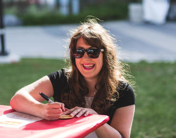 A woman at Alumni Weekend. She is crouched down at a table, wearing sunglasses and smiling